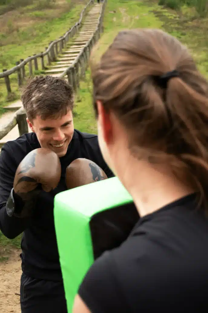 Trainer Mijnke Hoek begeleidt persoon tijdens bokscoaching sessie in de buitenlucht.