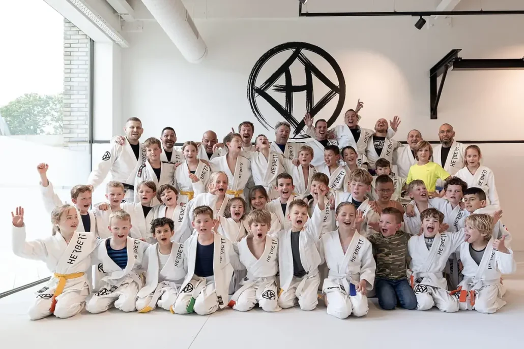 Judo voor kinderen: de complete oudergids 9 Grote groep lachende kinderen in judopak met hun docenten in de nieuwe judozaal van Sportschool Herbert in Ede