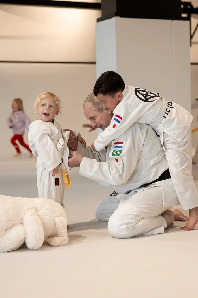 Slip op je judoband bevestigen: zo doe je het 1 Coach helpt kleuter met de judoband tijdens tuimeljudo Ede